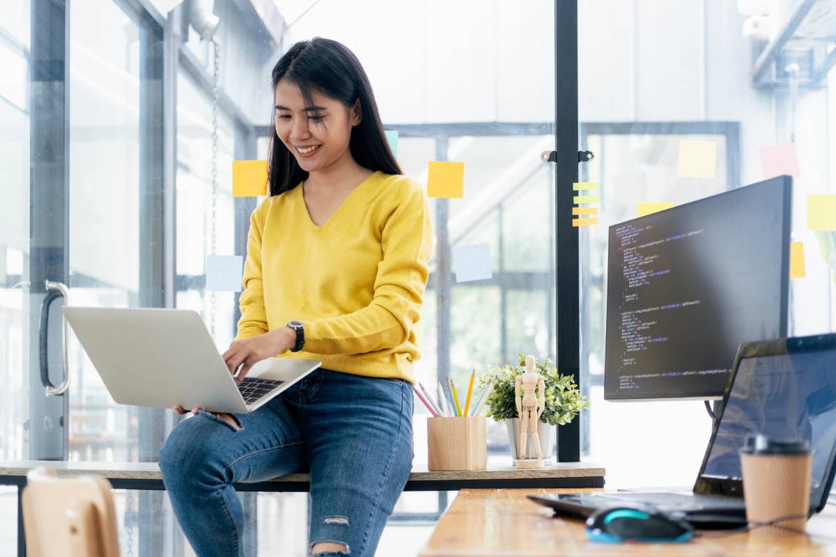 avantages-erp-entreprise-4 Femme souriante assise sur son bureau avec son ordinateur sur ses genoux