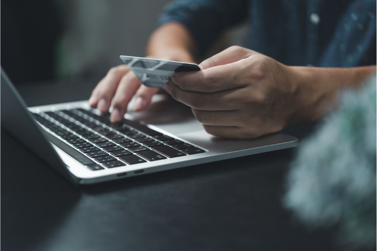 Homme tenant une carte de crédit devant son ordinateur parce qu'il fait un achat en ligne sur un e-commerce