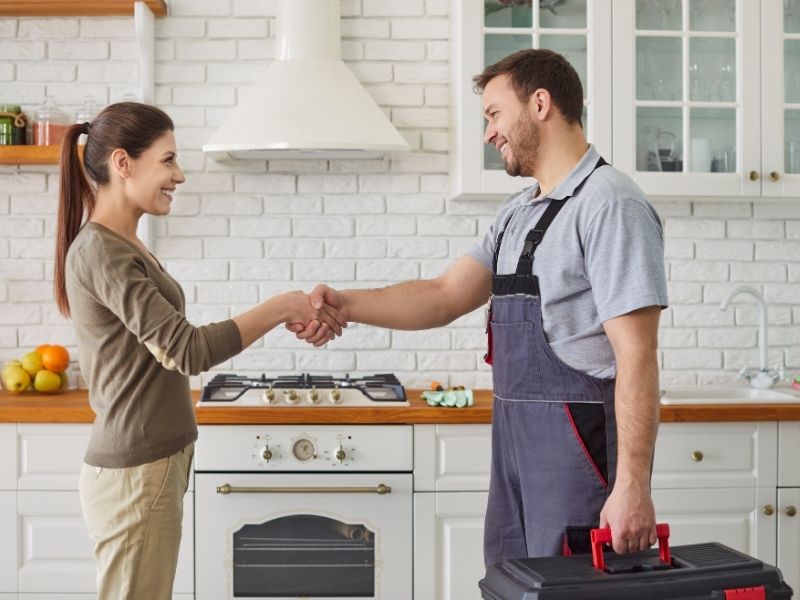 Technicien plombier serrant la main de sa cliente après avoir réparé son evier